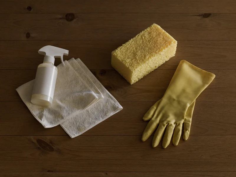 Aufsicht auf neutrale Reinigungsutensilien wie Mikrofasertücher, Sprühflasche, Schwamm und Handschuhe